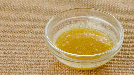 Mix of melted butter and garlic seasoning close-up in a glass bowl on a kitchen table in rustic background