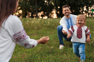 Happy parents in embroidered Ukrainian shirts playing with their cute daughter outdoors