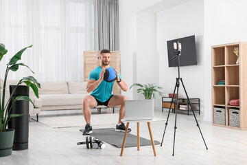 Fototapeta na wymiar Trainer with ball streaming online workout on phone at home