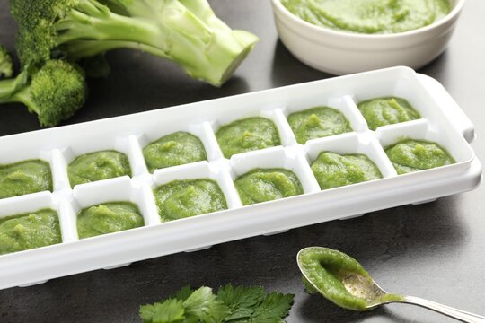 Broccoli puree in ice cube tray and ingredients on grey table, closeup. Ready for freezing