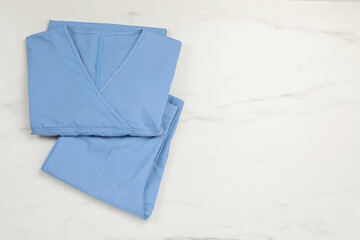Light blue medical uniform on white marble table, top view. Space for text