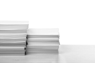 Stacks of paper sheets on light wooden table against white background. Space for text