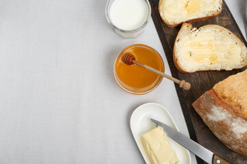 Sandwiches with butter, honey and milk on white table, flat lay. Space for text