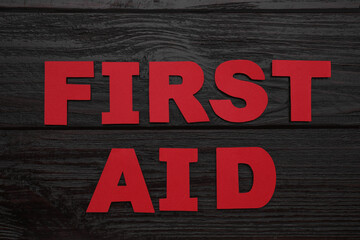 Words First Aid made of red letters on black wooden table, flat lay