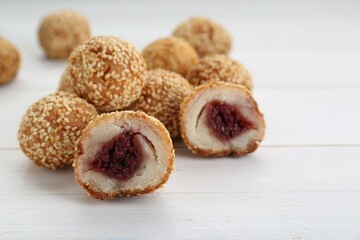 Delicious sesame balls with red bean paste on white wooden table, closeup