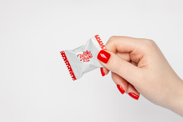 Woman's hand with red manicure, holding a candy with love lettering, isolated on white, Valentine's Day concept, copy space.