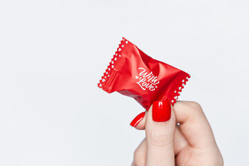 Woman's hand with red manicure, holding a candy with love lettering, isolated on white, Valentine's Day concept, copy space.