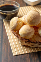 cheese breads in wooden basket with cup of coffee, concept of traditional brazilian meal, afternoon snack, vertical photo