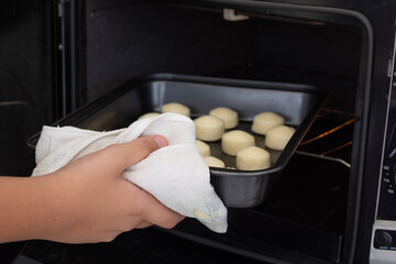 Fototapeta na wymiar man placing baking sheet with raw cheese bread inside an electric oven (or pão de queijo in portuguese)