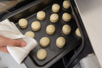 man placing baking sheet with raw cheese bread inside an electric oven (or p&atilde;o de queijo in portuguese)