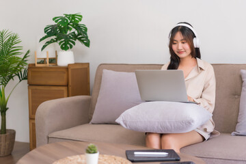 Relaxation lifestyle concept, Young Asian woman is wearing headphone and watching movie on laptop