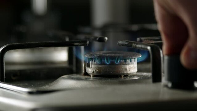 close up view of turning on gas stove, defocused hand turns gas supply valve and lights burner in kitchen in morning. concept of cooking and tea or coffee.
