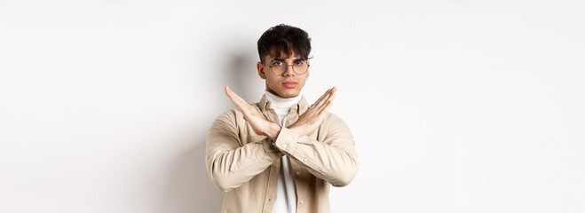 Image of serious young guy in glasses say no, showing cross gesture, make stop sign to disagree or...
