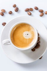 Fragrant coffee with foam in a white cup and grains scattered nearby. Traditional morning drink. Vertical. Top view. White background.