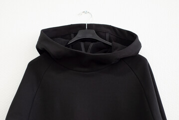 Stylish black sweater with a hood on a white background, front view. Urban clothing made of knitted footer hangs on hangers. Place for text. Mocap.