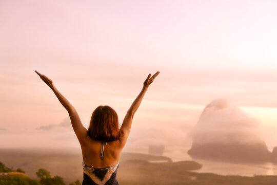Senior woman raising hands up in the air, feeling happiness, freedom, victory with small island in ocean background, breathing the pure ozone when traveling. Journey, lifestyle, love, victory concept.