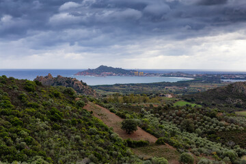 Fototapeta na wymiar View of Farm Fields and Town on the Sea Coast. Santa Maria Navarrese, Sardinia, Italy. Cloudy and Rainy Sky.