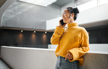 Phone call, communication and mockup with an asian woman talking while standing in a hallway. Mobile, networking and conversation with an attractive young female speaking on her smartphone indoor