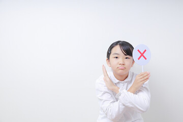 ✖️の札を持ったへの字口をする女子小学生