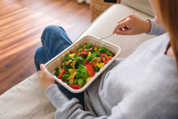 Closeup image of a young woman eating salad in paper box for takeaway food at home