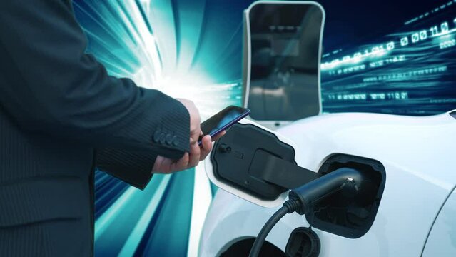 Progressive man check electric car's battery status with smartphone at charging station with technology background of binary code flying through votex. EV car concept with modern technology.