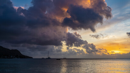 Fantastic tropical sunset. Purple and pink clouds in the sky illuminated by orange and gold. Silhouettes of yachts in the ocean. Reflections and glare on the water. Seychelles. Mahe