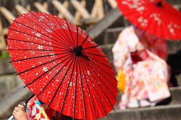 赤色の花柄の日傘を持った和装の後姿の人物です。