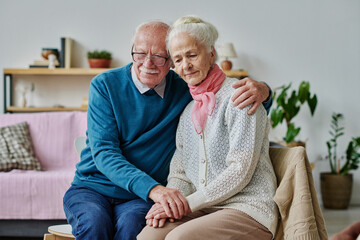 Senior man embracing his wife in depression and supporting her while they sitting on chairs in the...