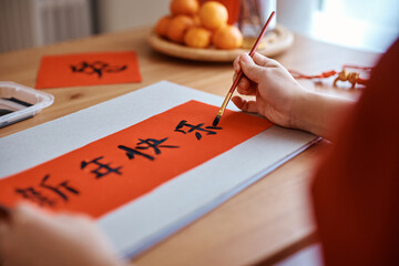 Close up of woman writing calligraphy on red rice paper while decorating her home for Chinese New...