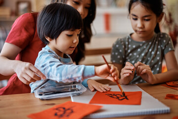 Small Chinese boy learning to write Fai Chun with his mother and sister at home.