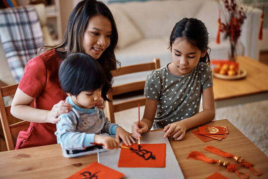 Asian family using ink while doing calligraphy on red piece of paper during Chinese New Year celebration.