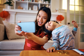 Carefree Chinese mother and son taking selfie during Lunar New Year celebration at home.