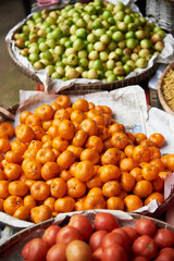 piles of mandarin oranges, monkey apples, and tomatoes on flat basket for sell in the market