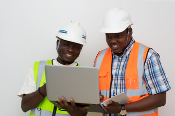 Portrait of two african industrial builders standing at building site and looking at laptop...