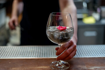 transparent cocktail in a glass decorated with a red flower on the bar counter
