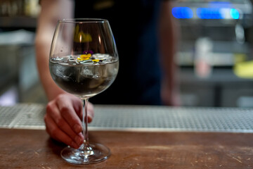 a transparent cocktail in a glass decorated with flowers in the hands of a barien
