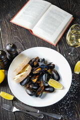 boiled mussels in a plate with lemon and bruschetta on a table with a book and a glass of wine vertical photo
