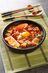 Sundubu jjigae is a Korean stew made with soft tofu, kimchi, pork belly, onion and spices closeup on the bowl on the table. Vertical