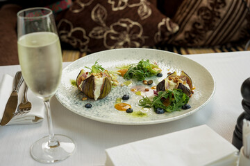 baked figs with cheese and pine nuts in a plate with salad on the table with a glass of white wine
