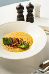 pumpkin cream soup with broccoli and mushrooms sprinkled with seeds in a white plate on the table with spices
