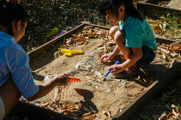 Cute little girl playing as a little archaeologist with her mother digging dinosaur fossils in the playground. Children learning about, Excavating dinosaur fossils simulation in the park.