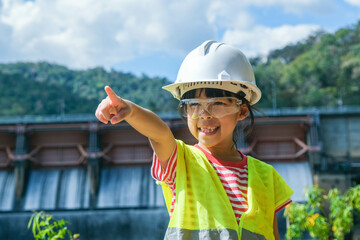 Portrait of a little girl engineer wearing a green vest and white helmet smiling happily on the...