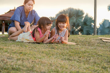 Fototapeta premium Happy sisters playing at the park slides down from the grassy hill sitting on a cardboard box. Happy children playing outdoors in summer. Family spending time together on vacation.