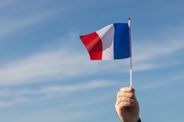 french flag in hand flutters in the wind against the sky