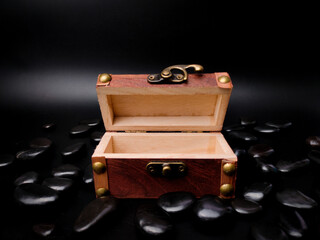 A mysterious open wooden chest surrounded by black stones is on a black background.