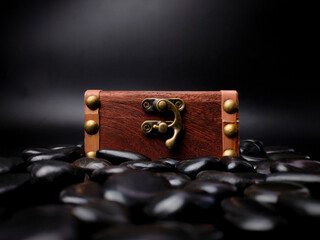 A locked mysterious wooden chest surrounded by black stones is on a black background.