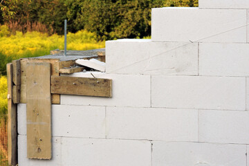 A construction pin, a reinforced concrete beam, steel bars and a wooden formwork on the first floor of a house under construction, walls made of autoclaved aerated concrete