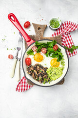 Fried scrambled eggs in a frying pan with avocado and mushrooms on a light background. Keto diet. vertical image. top view. place for text