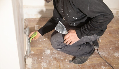 Worker is applying putty on a wall. Renovating house