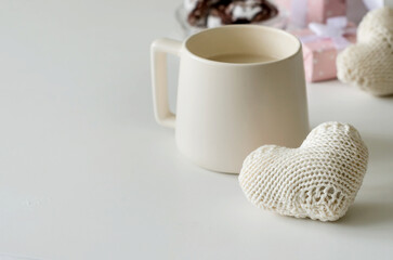 Obraz na płótnie Canvas White knitted heart, milk coffee cup and gift box on white table.